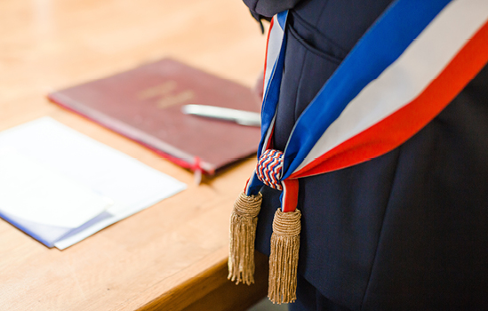 Veste du maire et écharpe tricolore devant un bureau avec un petit livret