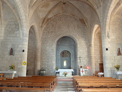 Nef d’église en pierre avec des arcs en pierre, un hotel et des bancs dans un village à la campagne